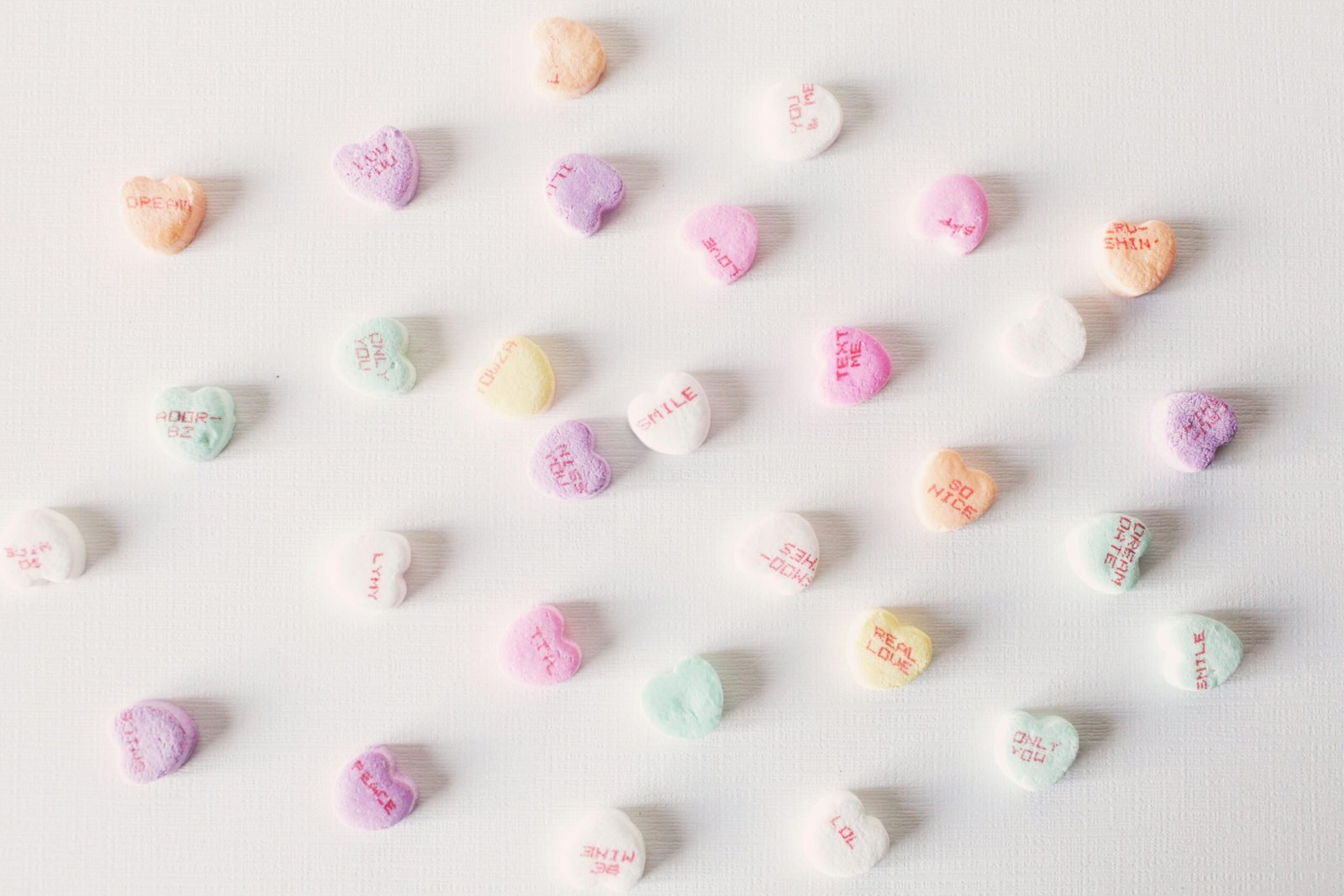 Top view composition of multicolored small heart shaped sweets placed on plain white surface